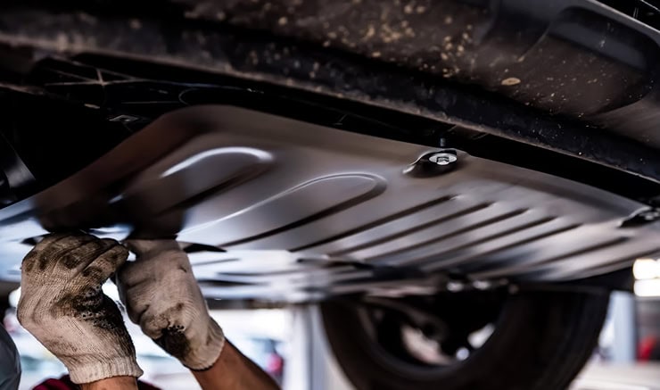 Imagen de reparación de coche, mecánico revisando la parte inferior del vehículo en taller especializado.